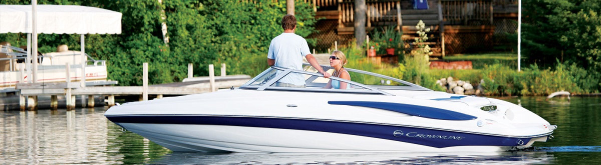 Couple standing in a Crownline boat docked in front of a log house